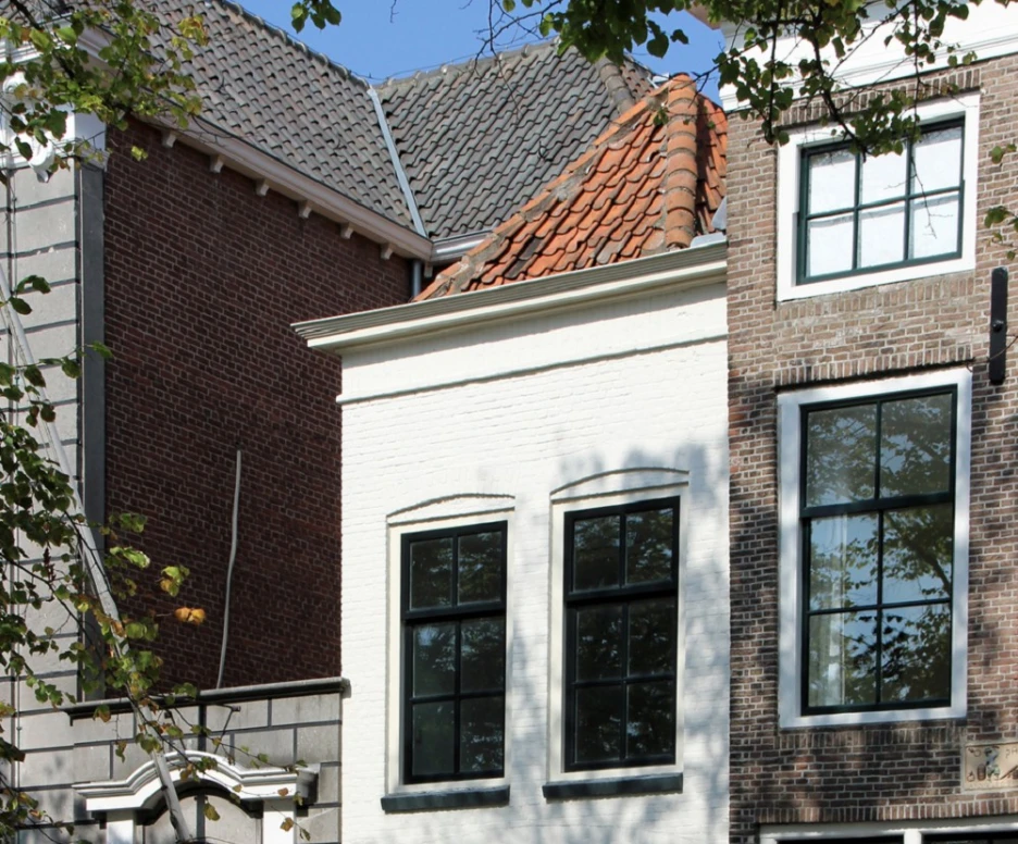 Two adjacent buildings with distinct architectural styles. The left side features a white facade with large windows, and the right side has a brick exterior with smaller windows. A door and a large window are visible on the white building, while the brick building has a prominent gabled roof. The scene is set under a clear blue sky, and autumn leaves can be seen on the ground.