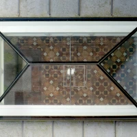 Ventana con marco geométrico muestra un suelo de azulejos de colores en un patrón decorativo. La vista es desde arriba, capturando la simetría del diseño.