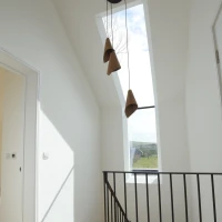 Helle Treppe mit Holzfußboden und schwarzem Geländer. Drei hängende Lampen aus Keramik. Großes Fenster lässt Tageslicht herein. Wände und Decken sind weiß gestrichen.
