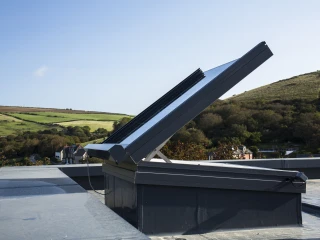 Panneau solaire incliné sur un toit, avec des collines verdoyantes en arrière-plan et un ciel bleu.