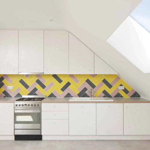 Cocina moderna con armarios blancos, una pared de azulejos en tonos amarillo, rosa y negro, y una ventana en el techo que permite la entrada de luz natural.