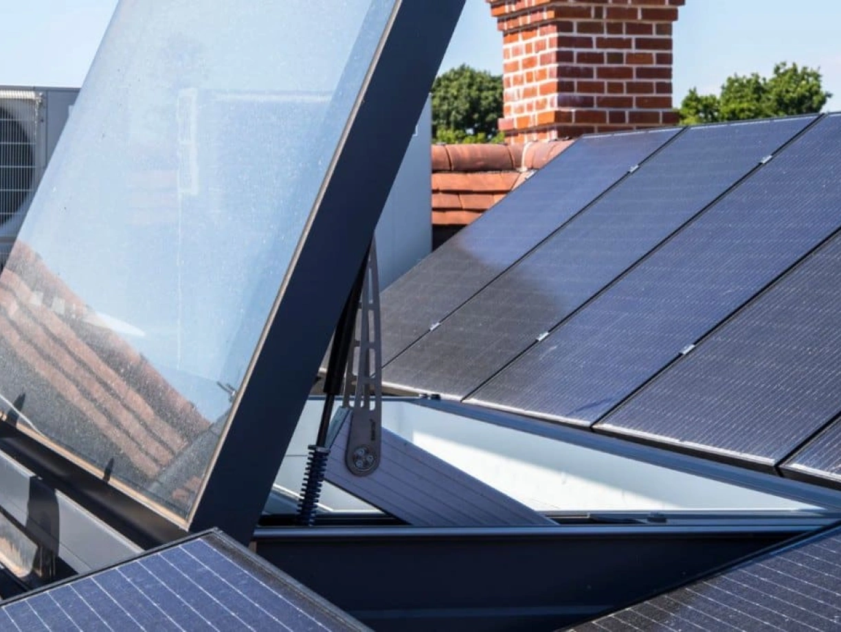 Panneaux solaires installés sur un toit, avec un couvercle en verre relevé dévoilant l’intérieur. Une unité de climatisation est visible en arrière-plan.