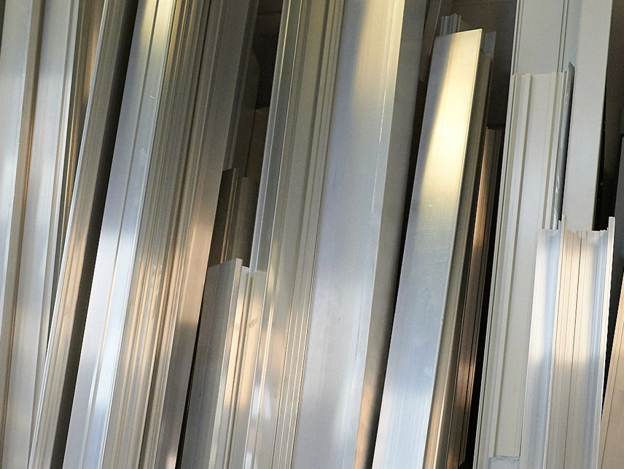Elementos de metal en láminas finas, apiladas desordenadamente. La luz refleja suavemente en su superficie, creando un efecto brillante.