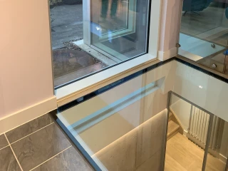 Großes Fenster zeigt die Außenseite eines modernen Hauses mit einem Spiegelbild der Person im Inneren. Der Boden ist aus Glas und gibt einen Blick auf die darunterliegende Ebene frei.