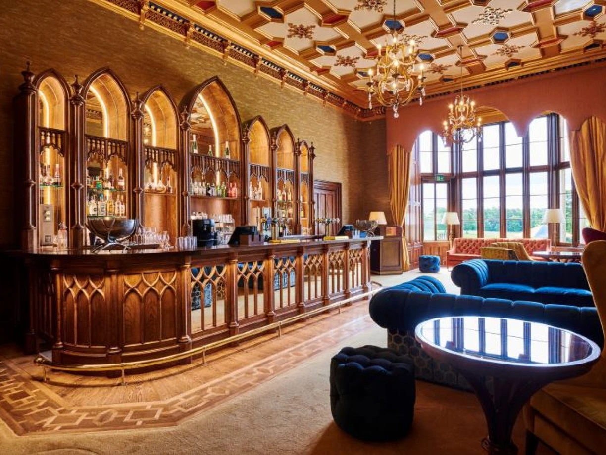Bar elegante con decoración de estilo gótico, mesas de madera y sillones cómodos. Grandiosas ventanas permiten la entrada de luz natural. Chandeliers brillantes adornan el techo adornado.