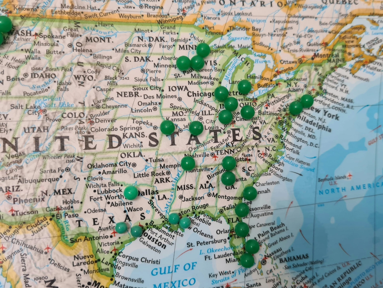 Eine Landkarte der Vereinigten Staaten mit vielen grünen Stecknadeln, die verschiedene Städte markieren. Die Karte zeigt auch die Ostküste und das zentrale Gebiet der USA.