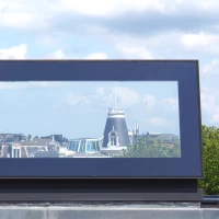 A rectangular window frame showcases a panoramic view of a city skyline with historical and modern buildings under a partly cloudy sky.
