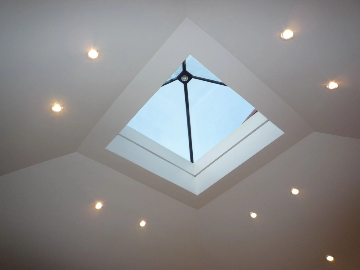 A modern ceiling with recessed lighting and a square skylight that shows a clear blue sky.