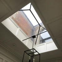 Plafond en panneaux avec un puits de lumière et un lustre noir moderne. La lumière naturelle éclaire l'espace intérieur.