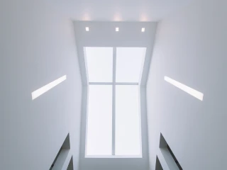 Blick nach oben in einen modern gestalteten Raum mit weißen Wänden und dreieckigen Fenstern, die Tageslicht hereinlassen. An der Decke befinden sich mehrere gleichmäßig verteilte Lichtquellen.