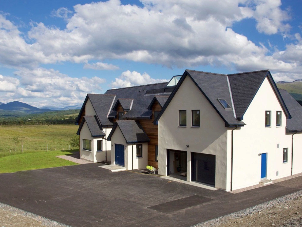 Maison moderne au style architectural unique, avec un revêtement blanc et des portes bleu vif. Située dans un paysage verdoyant, entourée de collines sous un ciel nuageux.