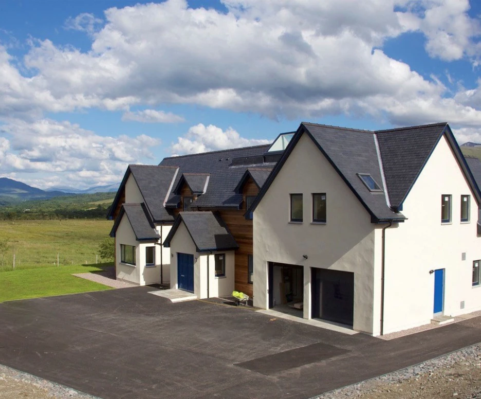 Maison moderne au style architectural unique, avec un revêtement blanc et des portes bleu vif. Située dans un paysage verdoyant, entourée de collines sous un ciel nuageux.