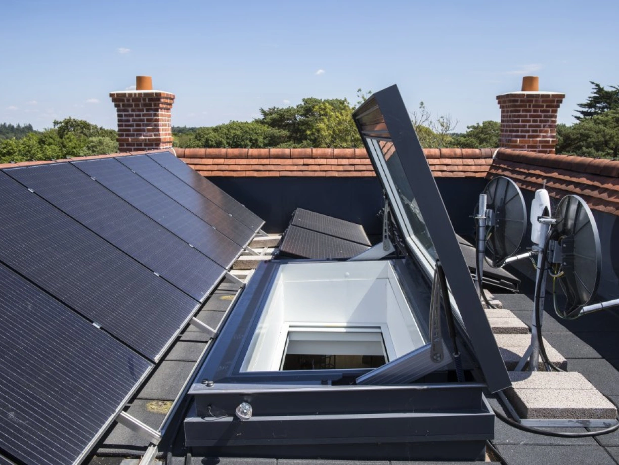 Techo con paneles solares y una claraboya abierta. También hay antenas parabólicas en la azotea, con un cielo azul despejado al fondo.
