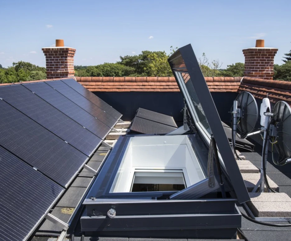 Techo con paneles solares y una claraboya abierta. También hay antenas parabólicas en la azotea, con un cielo azul despejado al fondo.