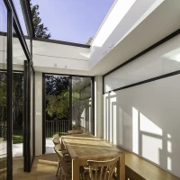 Comedor moderno con una mesa de madera clara y sillas de diseño sencillo. Las grandes ventanas permiten la entrada de luz natural y ofrecen vistas al jardín. Suelo de madera brillante y paredes blancas dan un aire minimalista al espacio.