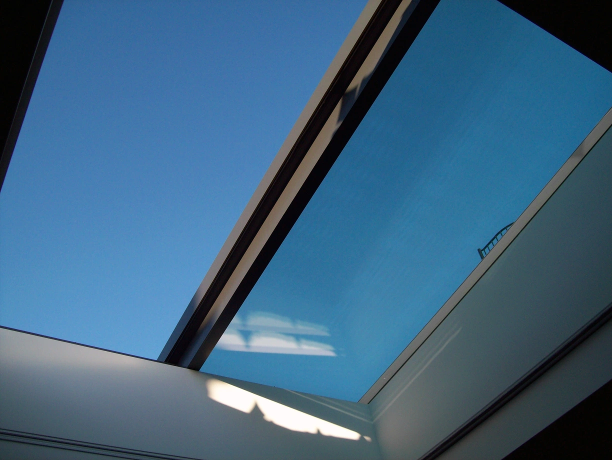 Vue d'un ciel bleu à travers un vitrage de toiture, avec des lignes géométriques créées par les bords du cadre.