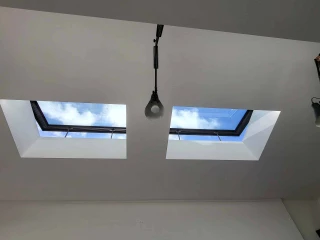 Two square skylights in a white ceiling, revealing a bright blue sky with clouds above. A light fixture hangs below one of the skylights.