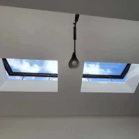 Two skylights in a white ceiling, showing a blue sky with scattered clouds. A single pendant light hangs below one of the skylights.