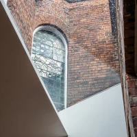 Vista de un espacio arquitectónico donde se combinan ladrillos expuestos y una ventana de cristal colorido. La luz entra a través de la ventana, iluminando las paredes.