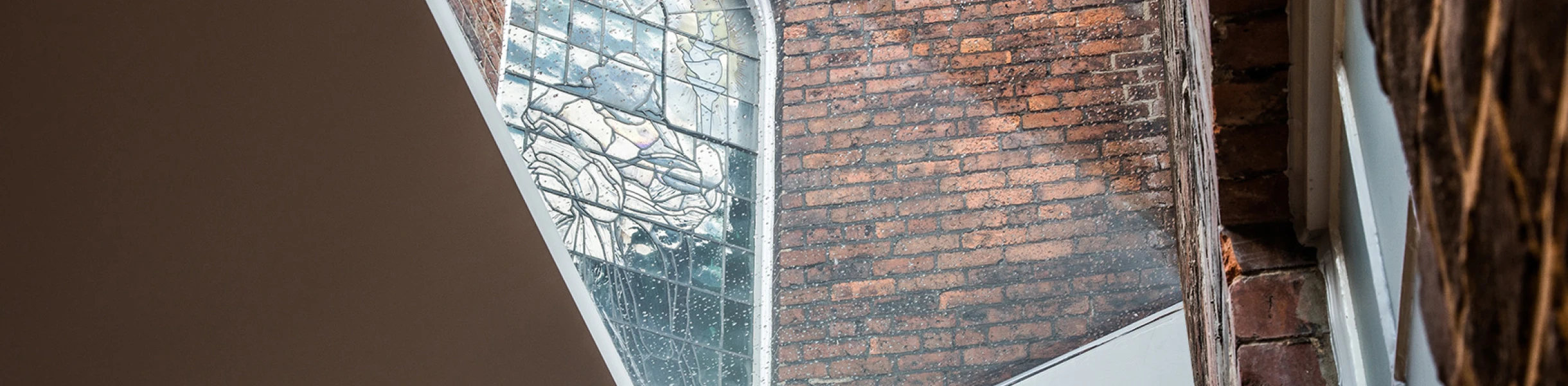 Vista de un espacio arquitectónico donde se combinan ladrillos expuestos y una ventana de cristal colorido. La luz entra a través de la ventana, iluminando las paredes.