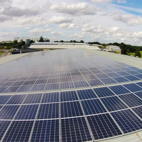 Solaranlage auf einem Dach mit vielen Photovoltaikmodulen. Im Hintergrund sind Gebäude und ein bewölkter Himmel zu sehen.